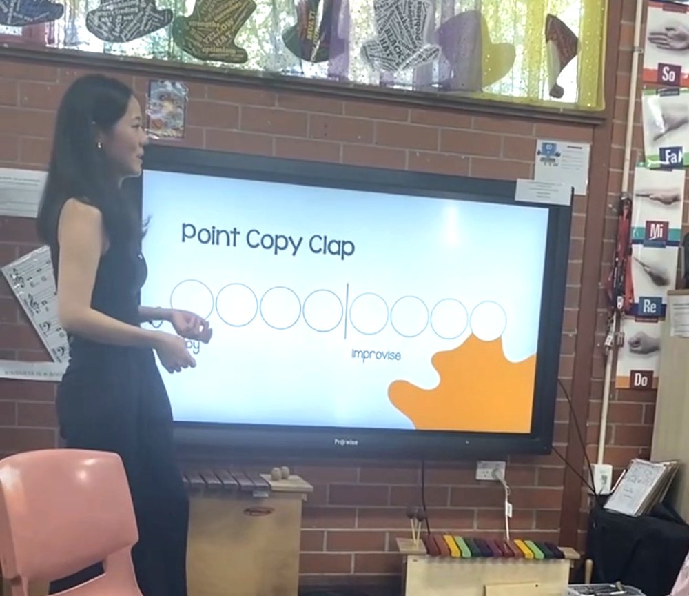 Nami Cheng teaching Point Copy Clap in front of the classroom screen